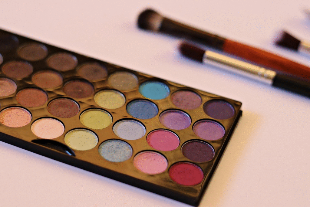 Paleta de sombras de ojos profesional con múltiples colores vibrantes y neutros, elaborada con micas para cosmética, junto a un set de brochas de maquillaje