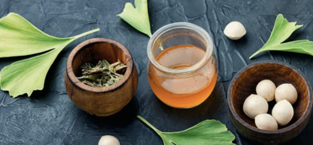 Composición de hojas frescas de Ginkgo biloba, semillas blancas en cuencos de madera y un frasco de vidrio con extracto líquido ambarino.