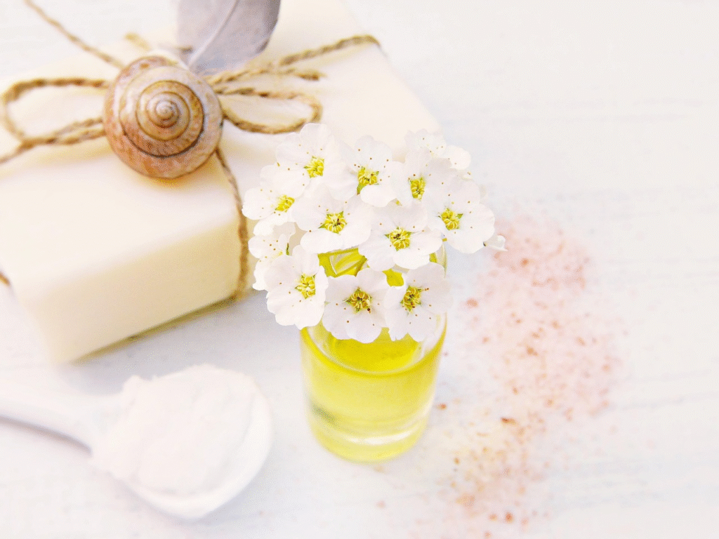 Ingredientes naturales para sales de baño caseras: aceite esencial con flores blancas, jabón artesanal, sales rosadas y polvo blanco en cuchara sobre mesa de madera