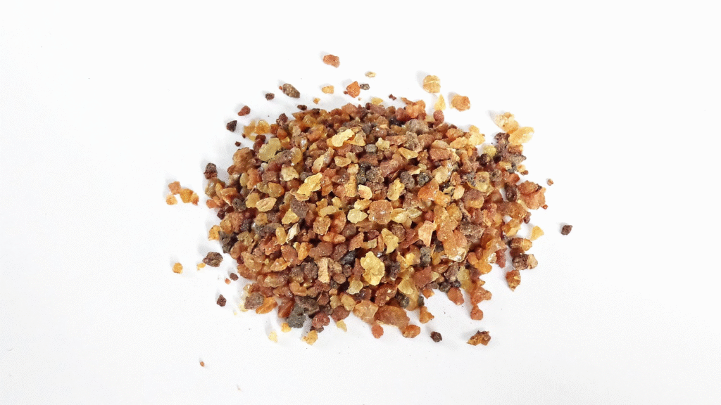 Pila de pequeños granos y cristales de resina de mirra de colores marrón y ámbar sobre un fondo blanco.