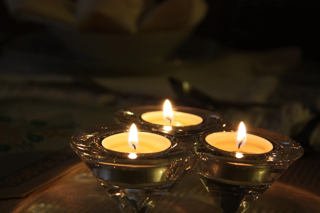 Tres velas de té encendidas en portavelas de vidrio transparente triangulares sobre una superficie de madera.