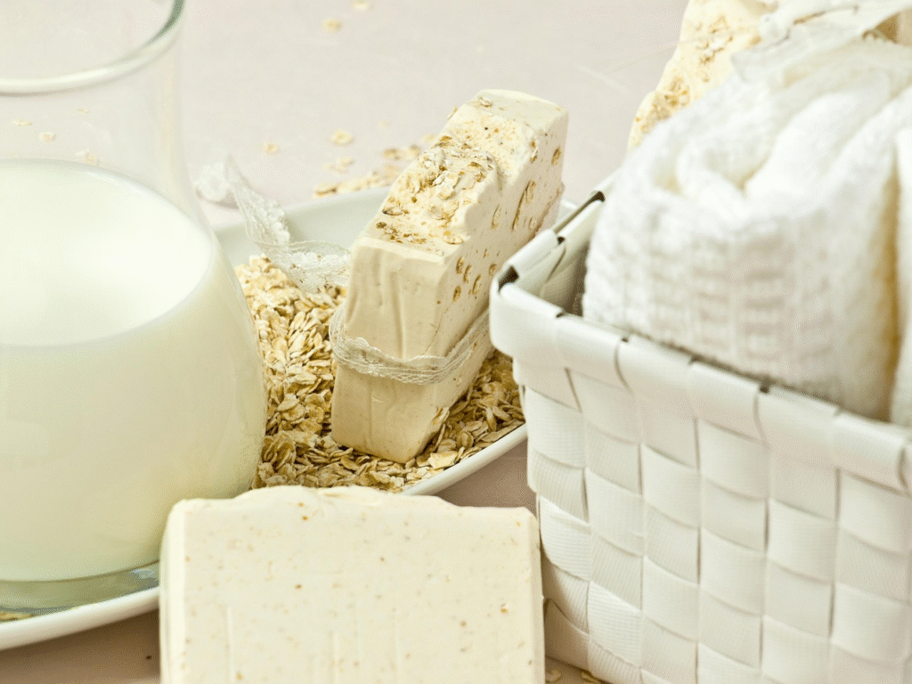 Primer plano de barras de jabón de avena natural y artesanal, con textura exfoliante y hojuelas visibles, junto a una jarra de leche. Ideal para ilustrar una receta de jabón casero hidratante.