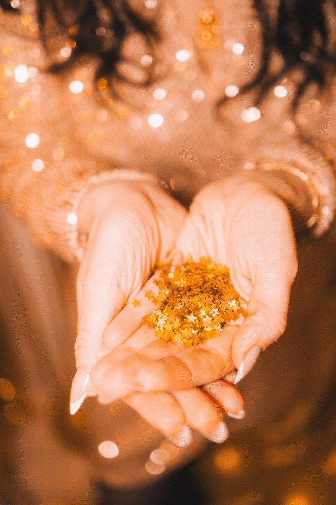 Manos sosteniendo glitter biodegradable en forma de estrellas doradas de Piñuela con fondo de luces festivas bokeh