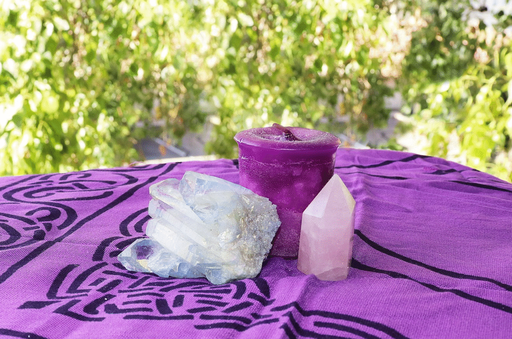 Vela morada para ritual de transmutación junto a cuarzo aura y punta de cuarzo rosa sobre mantel de altar violeta