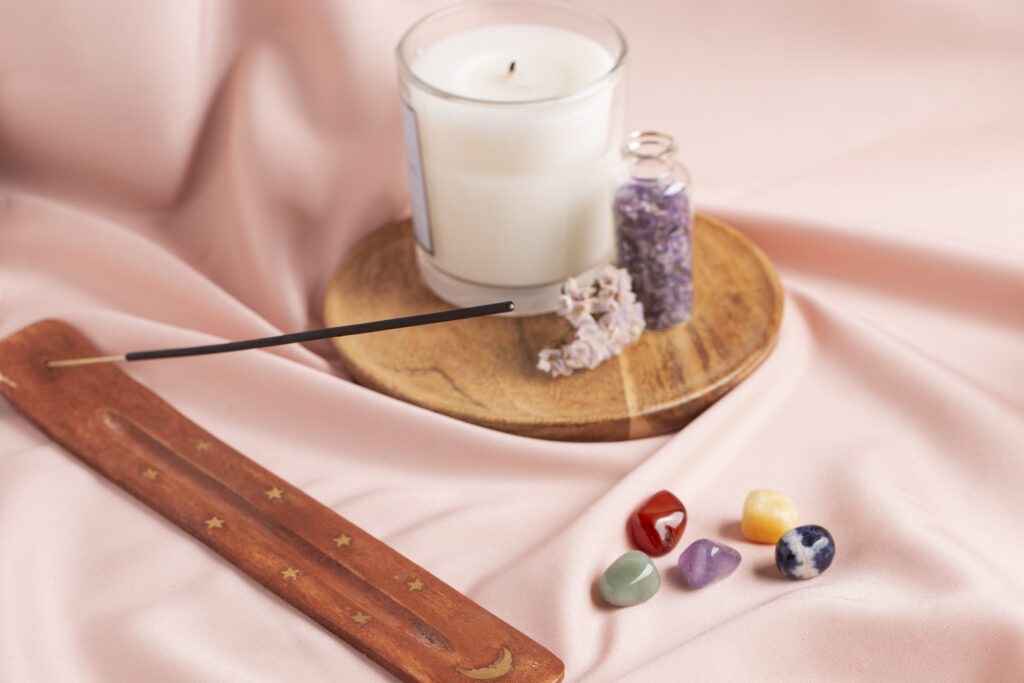 Kit de ritual holístico con vela blanca de cuarzos, varita de incienso en portainciensos de madera, piedras de los chacras, lavanda seca y flores sobre tela rosa